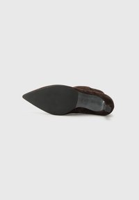Chaussure à talon haut en daim marron avec un bout pointu et une semelle noire lisse. Le design présente une texture subtile et des embellissements minimaux.
