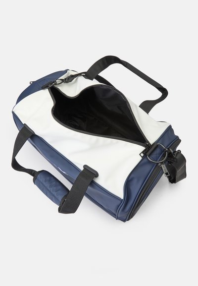 Mala de desporto com um exterior branco e azul-marinho, apresentando alças pretas ajustáveis, fecho com zíper e uma superfície lisa e brilhante. Interior preto visível.