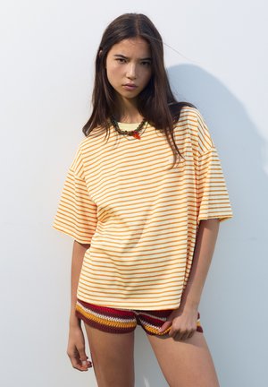 T-shirt surdimensionné à rayures jaunes et orange avec des manches courtes, associé à un short au crochet multicolore présentant un motif derayures ondulées.