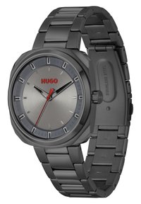 Reloj de acero inoxidable negro con caja redonda y esfera gris. Acentos rojos en el nombre de la marca y el segundero. Los eslabones de la correa son brillantes.