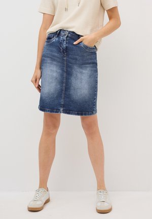 Denim skirt, dark blue, knee-length, straight cut, features belt loops, front pockets, and light fading along the fabric. Paired with sneakers.