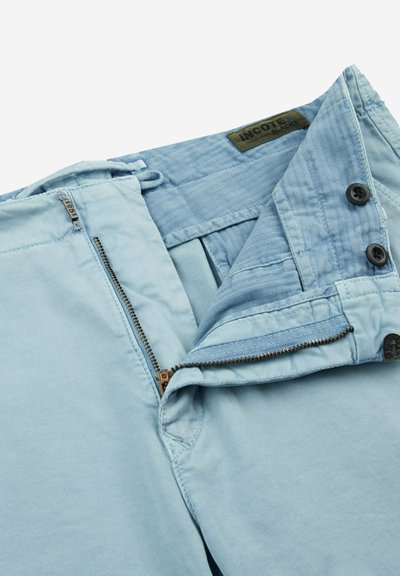 Pantaloni in cotone azzurro chiaro con zip, due bottoni scuri e una texture liscia. L'interno presenta una fodera in tessuto a contrasto.