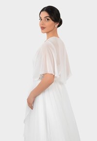 White dress with sheer, fluttery sleeves, layered tulle skirt, and a floral lace accent at the waist. Smooth texture and elegant design.