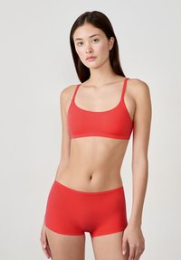 Set di un bralette e boyshort rosso senza cuciture, con spalline regolabili, texture liscia e design minimalista senza hardware visibile.