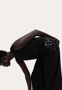 Top negro sin mangas con un dorso adornado con lentejuelas, combinado con pantalones negros sueltos. Textura de tejido suave, diseño simple.