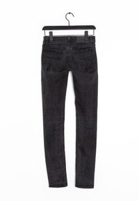 Svarta slim-fit jeans i denim, med femficksdesign, minimal sömnad och en slät yta. Hänger på en svart krok.