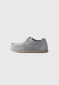 Chaussure décontractée en suède gris clair, à lacets, avec semelle en caoutchouc, talon bas et design moc toe cousu sur fond clair.