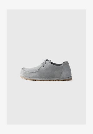 Lichtgrijze suède casual veterschoen met rubberen zool, lage hak en gestikte moc-toe design op een effen lichte achtergrond.