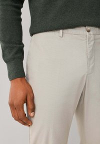 Pantalones beige claro con una textura suave y un ligero brillo, combinados con un suéter verde oscuro con un tejido de punto texturizado.