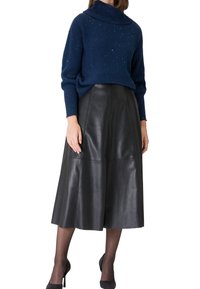 Mujer vestida con un suéter de cuello alto de canalé azul y una falda midi de cuero negra, combinada con medias negras transparentes y tacones negros.