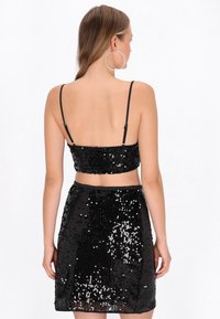 Fekete flitteres kétdarabos szett, mely rövidített, vékony pántos felsőből és hozzá illő szoknyából áll. A sima textúra fokozza a csillogást.