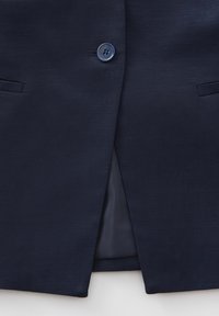 Marineblaue Blazer aus strukturiertem Stoff, mit einem einzelnen Knopfverschluss, zwei Fronttaschen und einem mittigen Schlitz auf der Rückseite.