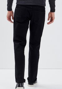 Schwarze Denim-Jeans mit schlanker Passform, Fünf-Taschen-Design und subtilen Nähten an den hinteren Taschen. Sie haben einen sauberen Abschluss und umgeschlagene Säume.