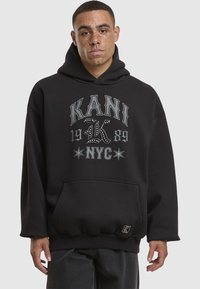 Sudadera con capucha negra hecha de tela suave, con una gran impresión gráfica que incluye texto y estrellas. Incluye un bolsillo frontal y puños acanalados.