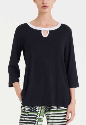 Top nero con scollatura rotonda bianca e dettaglio a chiave, maniche 3/4 e vestibilità rilassata, abbinato a pantaloni verdi e bianchi con motivo.