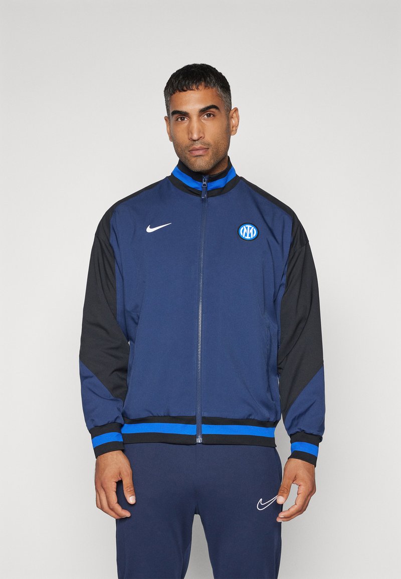 Giacca a zip navy e nera con accenti blu, caratterizzata da un logo brandizzato e polsini a costina. Realizzata in un tessuto morbido e leggero.