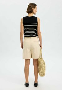 Top senza maniche a righe bianche e nere, pantaloni corti beige, con una borsa intrecciata. Tessuto morbido, design casual, dettagli minimi e colori neutri.