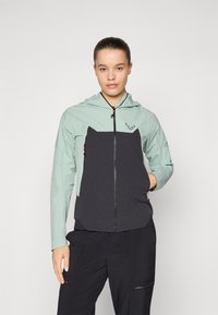 Kapuzejacke mit einem hellgrünen Oberteil und dunklem Marineblau am Körper, Reißverschluss und durchbrochenen Details für Belüftung und ein modernes Design.