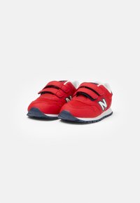 Baskets de sport rouges en matériau mesh et synthétique, dotées de deux straps en Velcro noirs, d'un intercalaires blanc et de semelles en caoutchouc bleu marine.