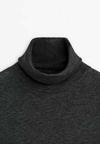 Pull à col roulé noir avec texture côtelée, coupe ajustée et tissu doux. Vue en gros plan du col et de la zone des épaules.