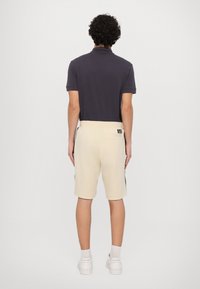 Camisa polo en azul marino oscuro, pantalones cortos en beige con franjas laterales oscuras, tela suave, corte relajado, parche de logo en el bolsillo trasero, zapatillas blancas.