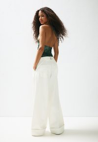 Green satin halter top with an open back, paired with wide-leg white trousers featuring a belt and pockets, on a plain white background.
