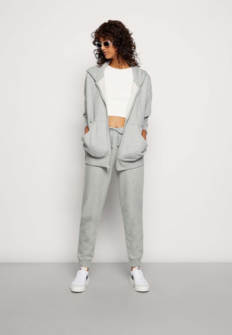 Ensemble de sweat à capuche gris et de joggings assortis. Tissu doux, coupe décontractée, poches avant et cordon de serrage ajustable. Top court blanc et baskets.