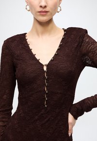 Burgundy lace dress with long sleeves, V-neckline, decorative buttons at front, and floral pattern. Textured fabric with a fitted silhouette.