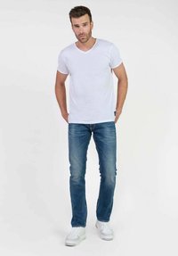 Camiseta blanca de cuello en V, jeans azules y zapatillas blancas. Jeans de corte recto, de lavado medio con un desvanecimiento sutil. Diseño simple y casual.