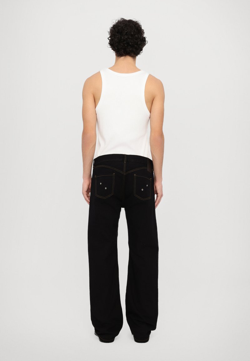 White tank top paired with loose-fitting black jeans. The jeans feature back pockets with visible stitching and rivets. Plain background.