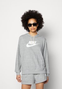 Felpa grigia leggera con tasca frontale e logo Nike bianco. Abbinata a pantaloni corti grigi coordinati, con vita elastica e texture liscia.