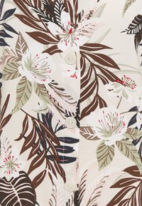 Chemise en tissu léger à motif floral avec un fond beige, des feuilles marron et vertes, des fleurs roses et des boutons blancs.