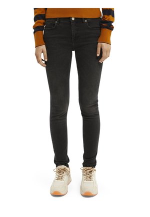 Person wearing black skinny jeans, orange and navy striped sweater, and white sneakers with orange soles, standing facing forward.