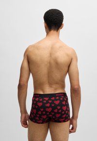 Boxer cortos negros con patrones de corazones rojos, cinturilla elástica que presenta el logo "HUGO", textura de tela suave y diseño de pierna corta.