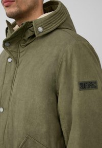 Olijfgroene jas met een gestructureerd oppervlak, geribbelde kraag, zilveren drukknoopsluitingen en een logo patch op de mouw. Voorzien van zijzakken.