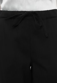 Black pants featuring a soft fabric, elastic waistband, and tied drawstring detail, with a smooth texture and clean design.