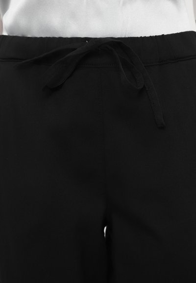 Mustad püksid, mis on valmistatud pehmest kangast, painduva paeltega vööst ja nööpide detailidega, sileda tekstuuri ja puhta disainiga.