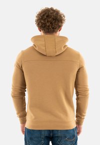 Felpa con cappuccio marrone, dalla texture liscia, con maniche aderenti e un'ampia apertura del collo, abbinata a jeans in denim blu.