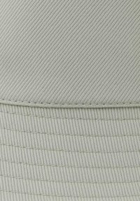 Cappello in tessuto grigio intrecciato con un design a coste e righe orizzontali. Presenta una visiera strutturata e cuciture a contrasto lungo le cuciture.