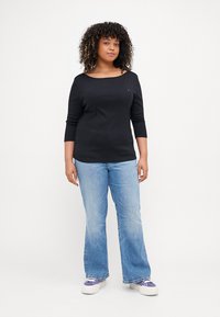 Svart båthals topp med trekvart ermer, parret med lyseblå utsvingte jeans. Sko med hvite såler og lilla detaljer.