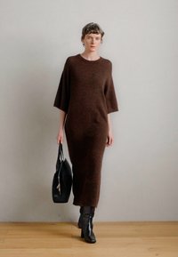 Garais brūns adīts kleita ar īsām piedurknēm, ar brīvu griezumu. Apvienots ar melniem ceļgala augstiem zābakiem un melnu somiņu.