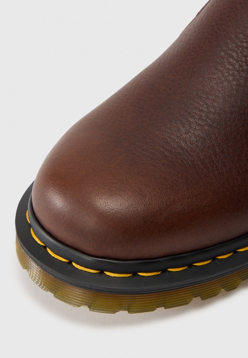 Brauner Lederstiefel mit runder Zehenform, strukturierter Oberfläche, schwarzer Plateausohle und gelben Nähten am Rand.