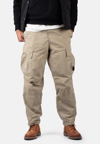 Pantalones cargo beige hechos de un material duradero, con múltiples bolsillos, un ajuste relajado y una textura ligeramente arrugada.