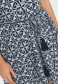 Suknja u mornarsko plavoj i bijeloj boji sa složenim cvjetnim uzorcima, strukirana pletenim remenom i resicama.