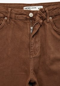 Brązowe dżinsy o luźnym kroju z zapięciem na zamek błyskawiczny i metalowym guzikiem. Metka z marką "Koton" oraz rozmiarem "W36". Teksturowana tkanina.