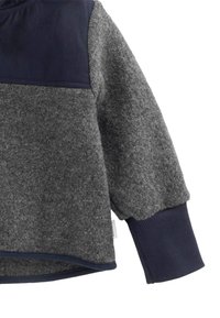 Grau Fleecejacke mit einem Ärmel in Marineblau und geripptem Bündchen sowie einer Schulterpatch, der die Textur des Stoffes und das geschwungene Saumdetail zeigt.