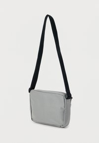 Γκρι υφασμάτινη τσάντα ταχυδρόμου με ορθογώνιο σχήμα, μαύρο ρυθμιζόμενο λουρί και κλείσιμο με φερμουάρ. Λεία υφή, ελάχιστες λεπτομέρειες.