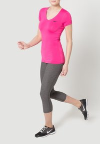 Fitted pink v-neck athletic shirt with short sleeves, paired with dark gray capri leggings and black athletic shoes featuring white accents.
