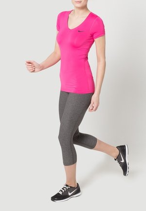 Fitted pink v-neck athletic shirt with short sleeves, paired with dark gray capri leggings and black athletic shoes featuring white accents.
