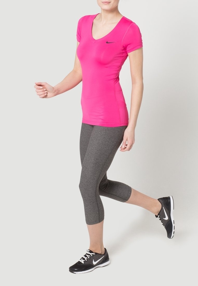 Fitted pink v-neck athletic shirt with short sleeves, paired with dark gray capri leggings and black athletic shoes featuring white accents.